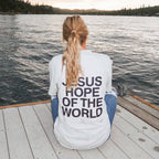 Person sitting on a dock by a lake wearing a shirt with 'Jesus Hope of the World' text.
