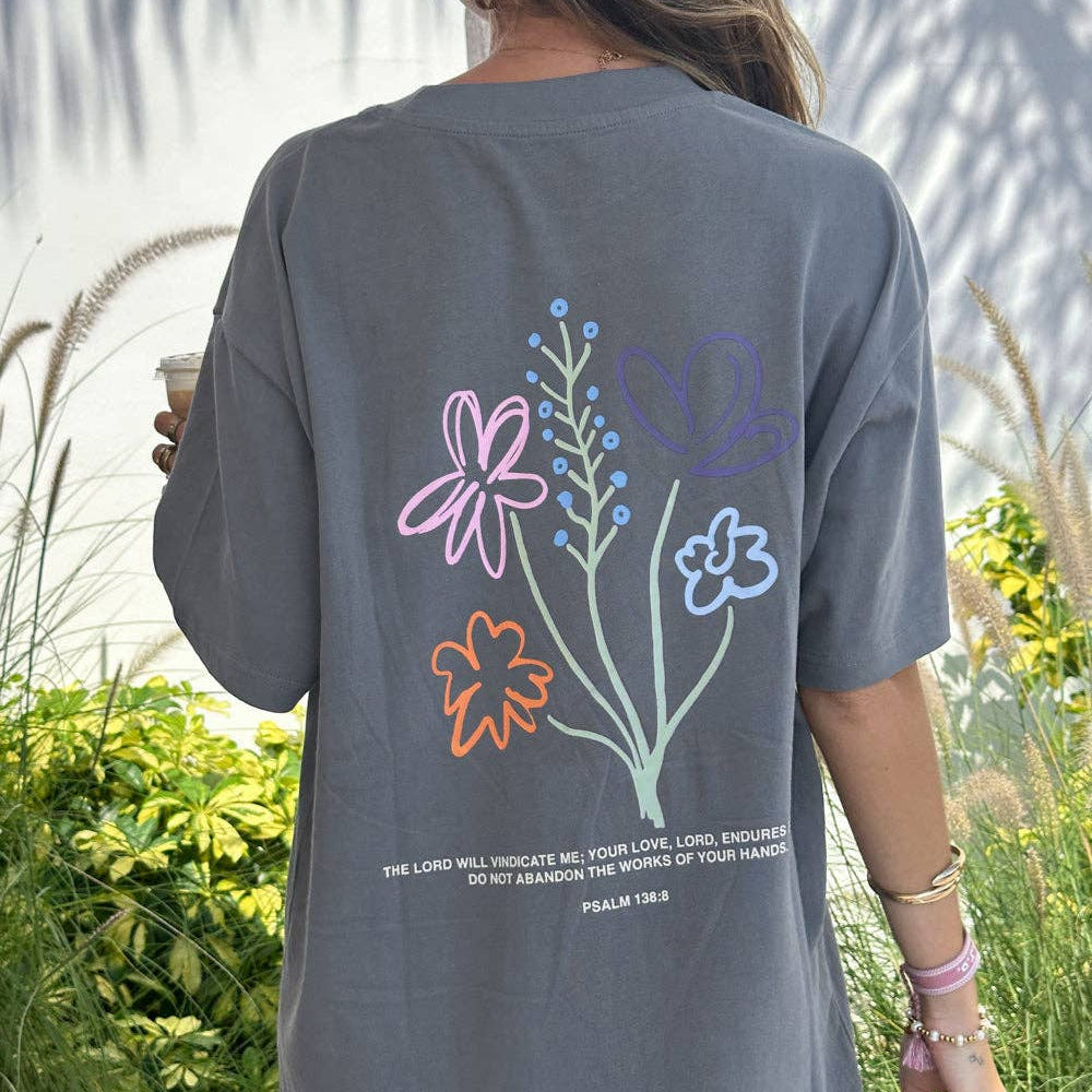 Person wearing a gray t-shirt with floral designs and text outdoors
