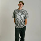 Person wearing a camo graphic t-shirt with 'Jesus Loves You' text on a plain background