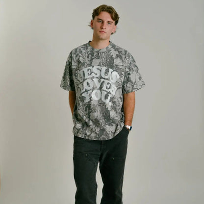 Person wearing a camo graphic t-shirt with 'Jesus Loves You' text on a plain background