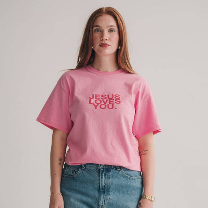 Person wearing a pink t-shirt with 'Jesus loves you' text on a plain background