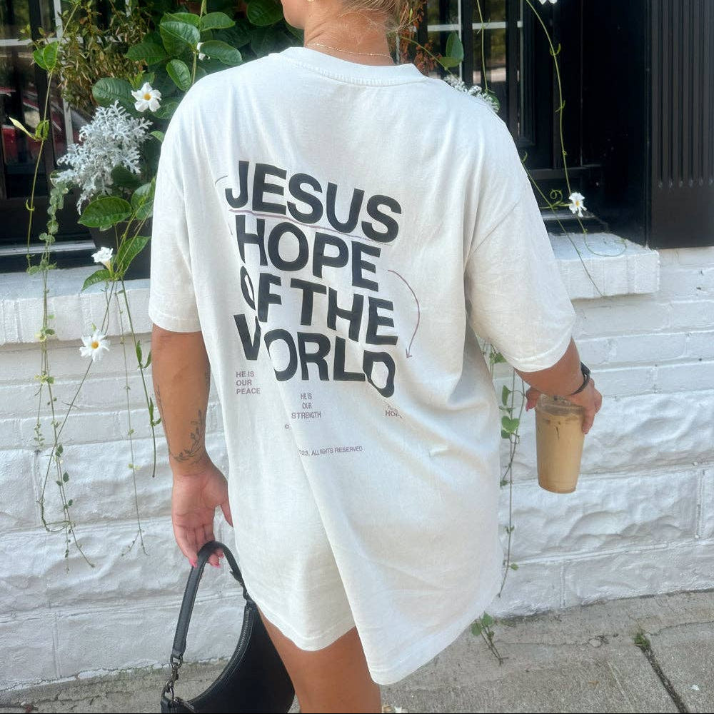 Person wearing a white t-shirt with 'Jesus Hope of the World' text, standing outdoors.