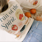 Two people wearing bags with 'Fruit of the Spirit' design, surrounded by oranges and a mesh bag.