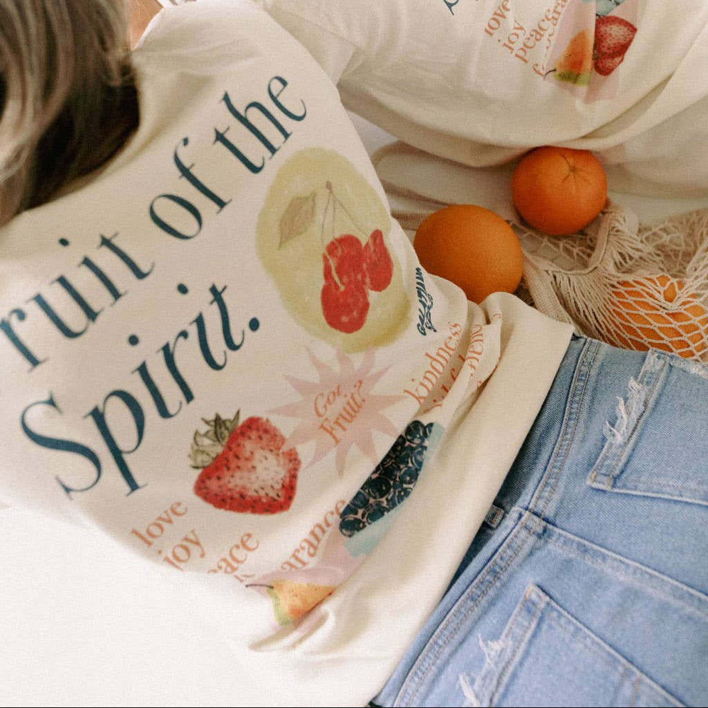Two people wearing bags with 'Fruit of the Spirit' design, surrounded by oranges and a mesh bag.