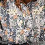 Two models wearing matching camouflage hoodies with the text 'JESUS LOVES YOU' printed in gold on the chest.