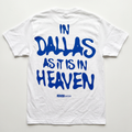 White short-sleeve t-shirt laid flat on a light background, featuring the phrase 'IN DALLAS AS IT IS IN HEAVEN' printed in large blue letters across the back, with 'HEAVEN below' in smaller blue text underneath.