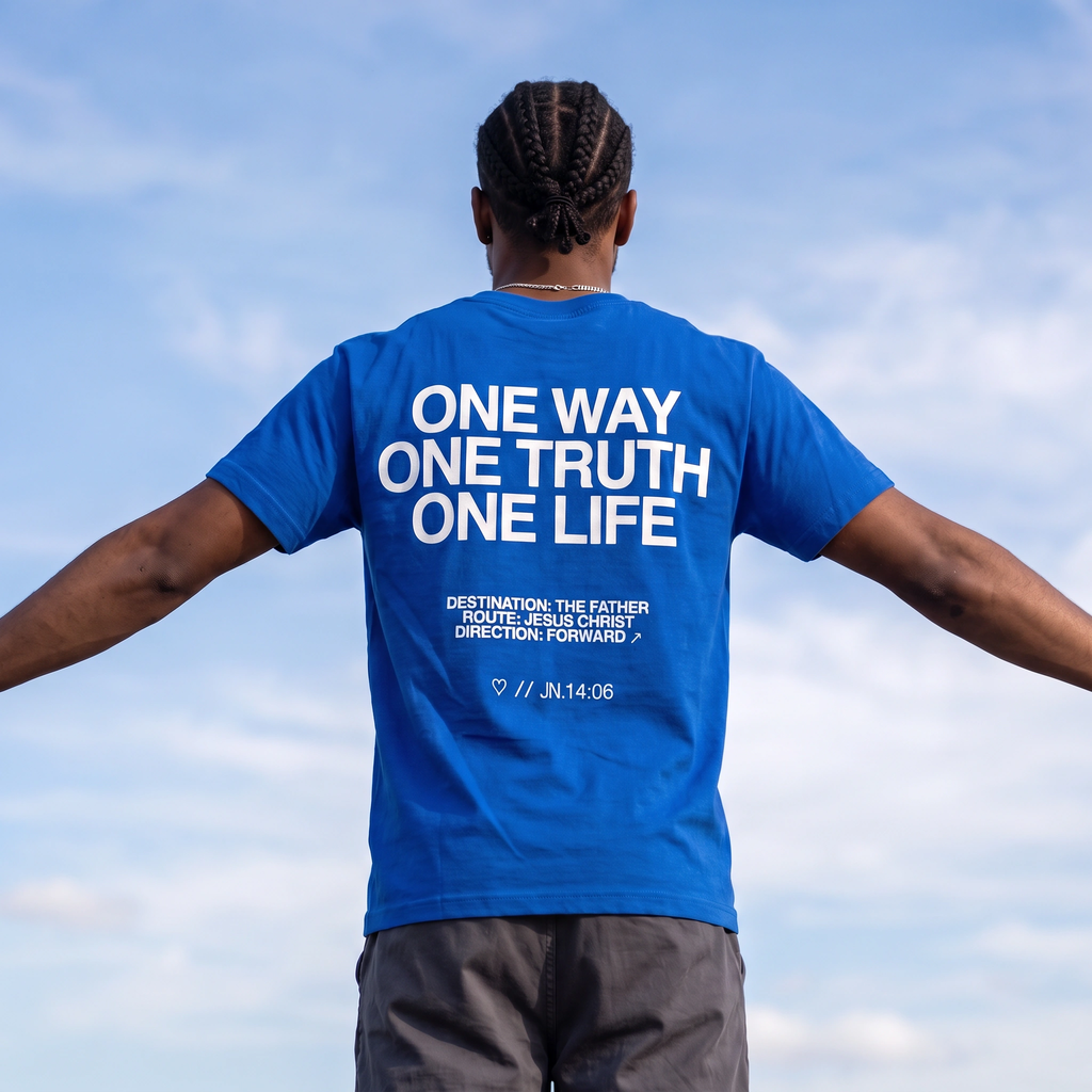 A man viewed from behind wearing a bright blue t-shirt with white text that reads 'ONE WAY ONE TRUTH ONE LIFE' and smaller scripture text below, set against a blue sky background.