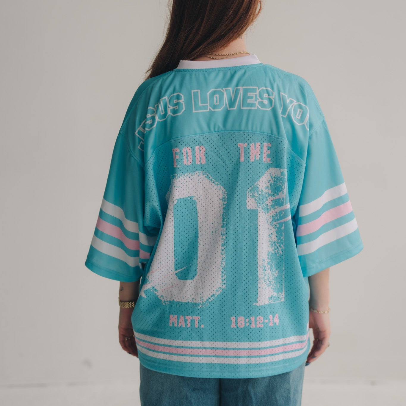 Person wearing a turquoise jersey with text and numbers on a plain background