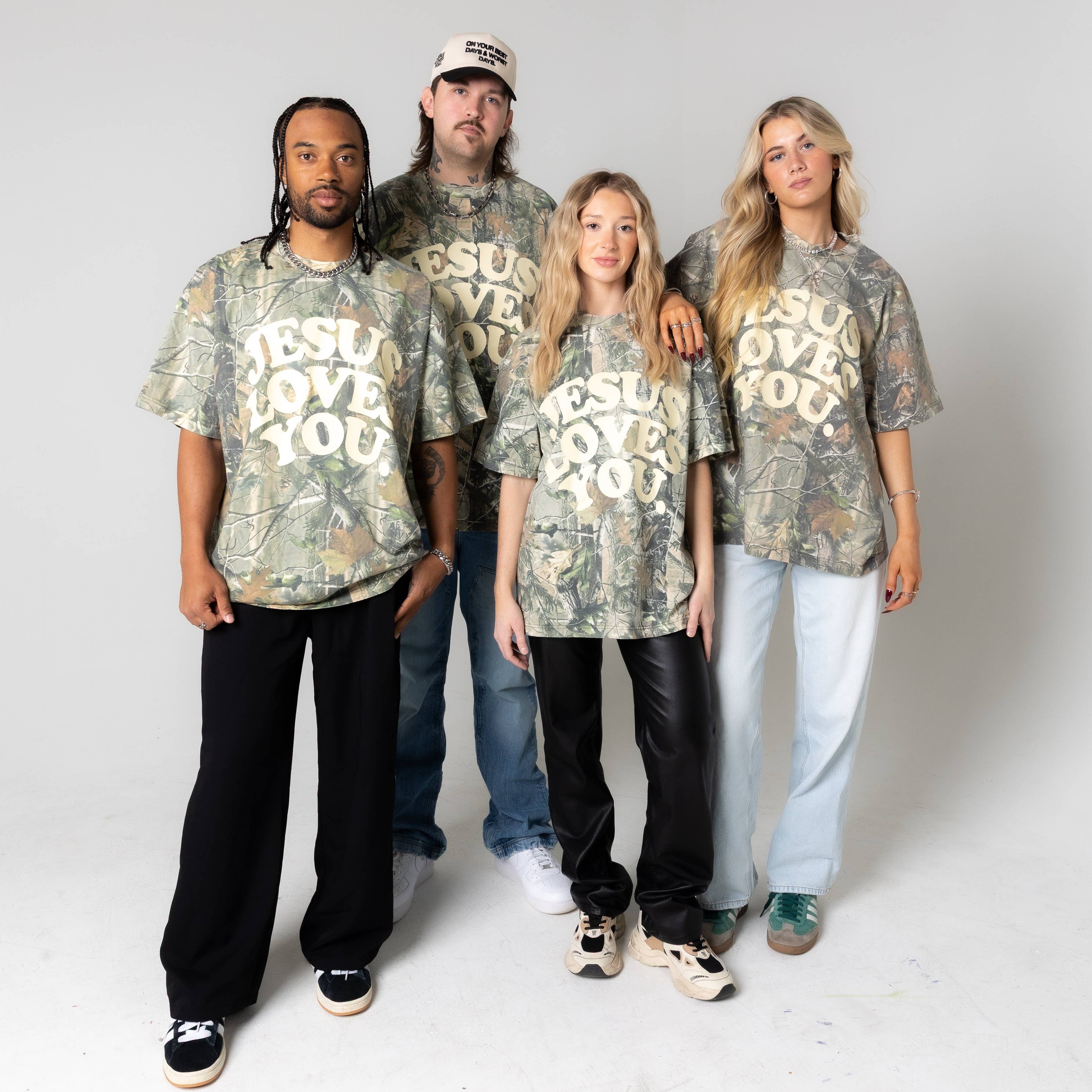 Four people wearing matching camouflage t-shirts with 'Jesus Loves You' text on a white background