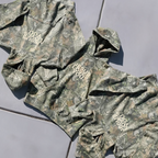 Three camouflage hoodies in green, brown, and beige tones are laid out on a gray tiled floor. Each hoodie features a white graphic text print on the chest, including 'DO NOT DISTURB' and 'JUST SHUT UP'.