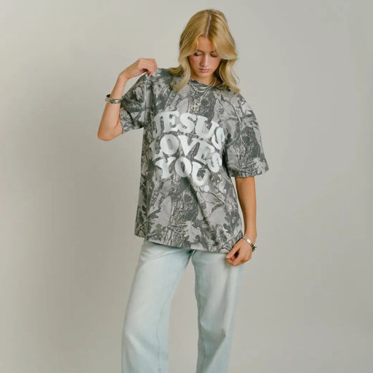 Woman wearing a come shirt with JESUS LOVES YOU text, light blue jeans, and red shoes on a plain background