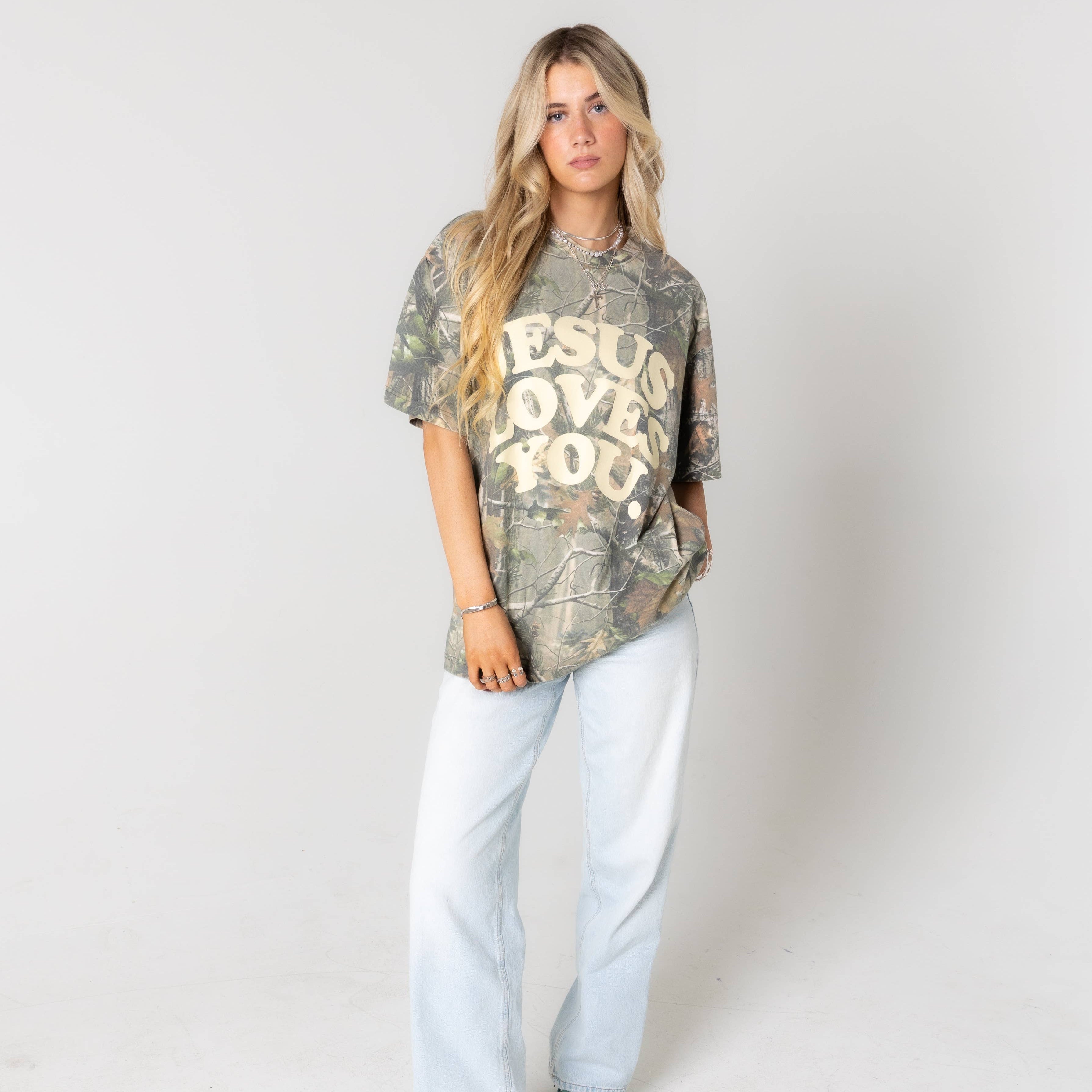 Woman wearing a camouflage t-shirt with 'Jesus Loves You' text on a white background