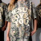 Person wearing a camouflage t-shirt with 'Jesus Loves You' text.