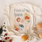 Beige tote bag with 'Fruit of the Spirit' text and illustrations on a light background with fruits.