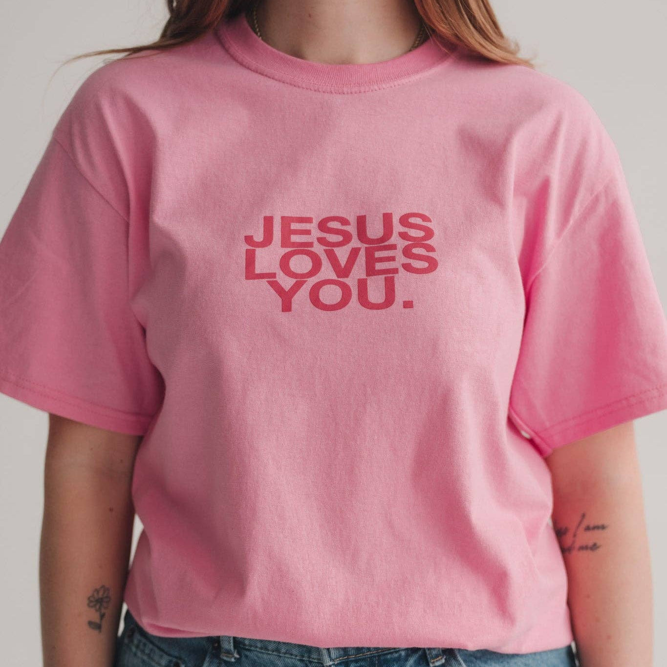 Person wearing a pink t-shirt with 'Jesus Loves You' text.